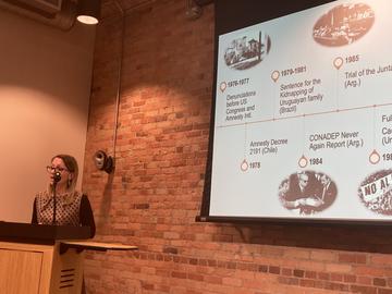 Dr Lessa standing behind a lectern and in front of a large presentation screen