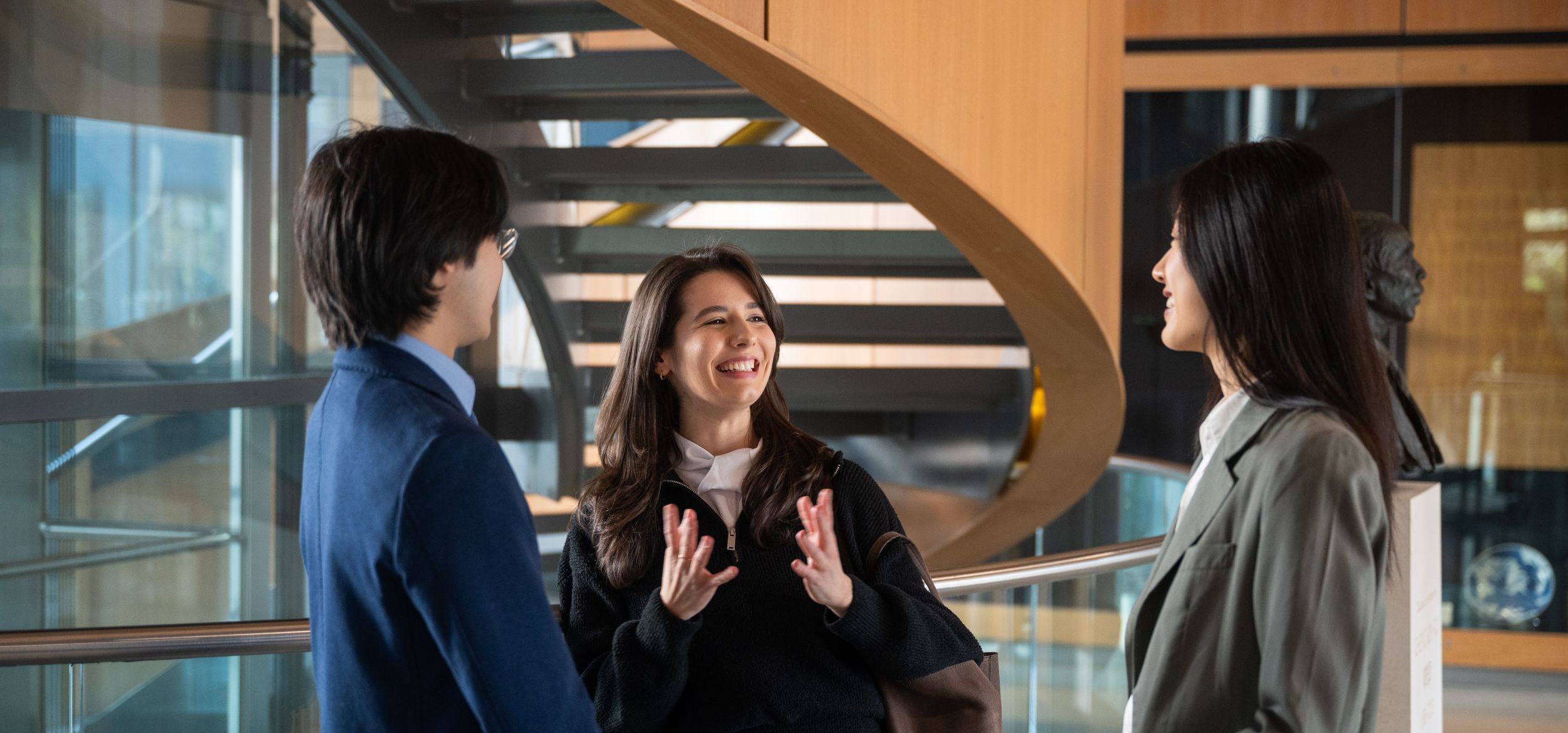 Three students standing inside college building talking and laughing