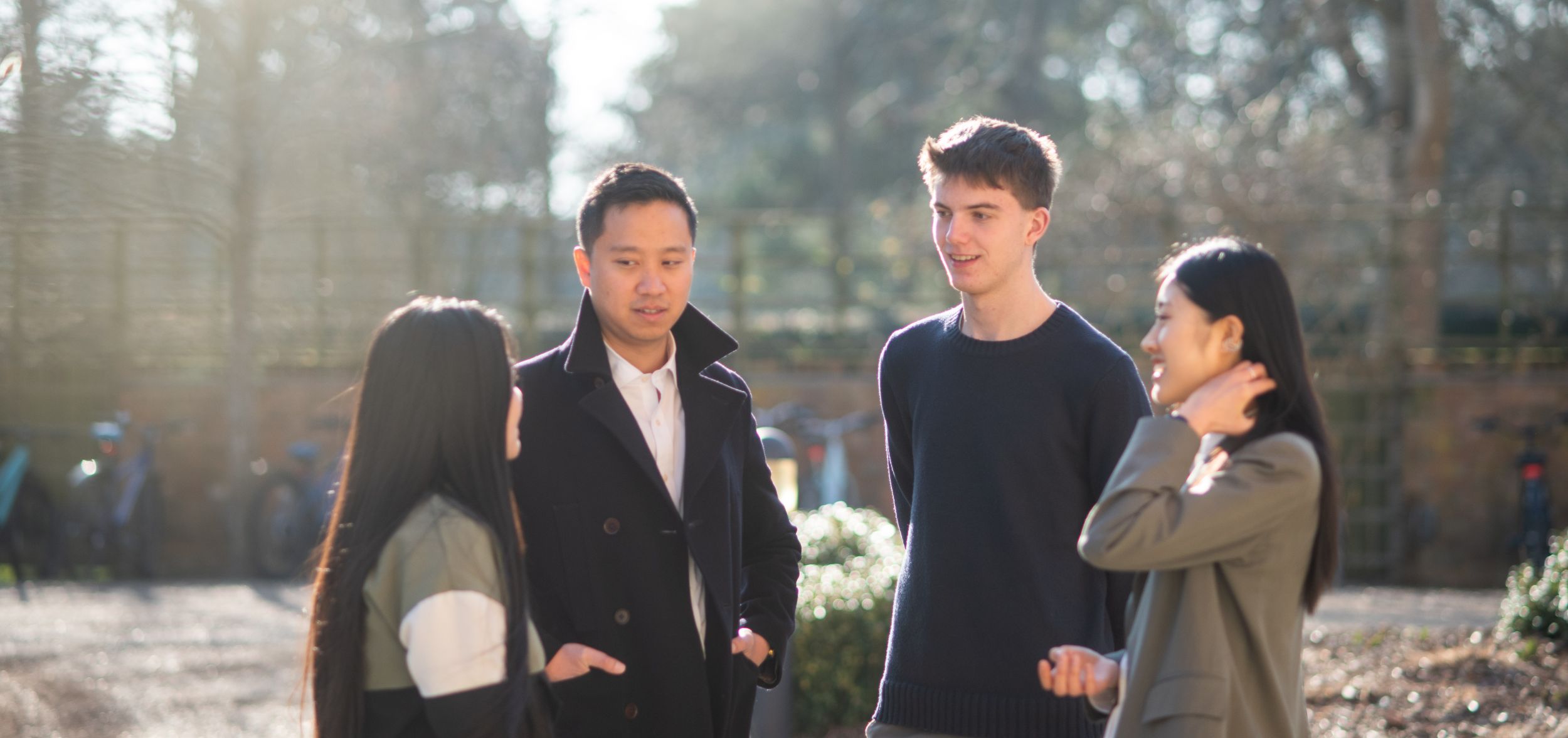Four students standing outside talking on a sunny day