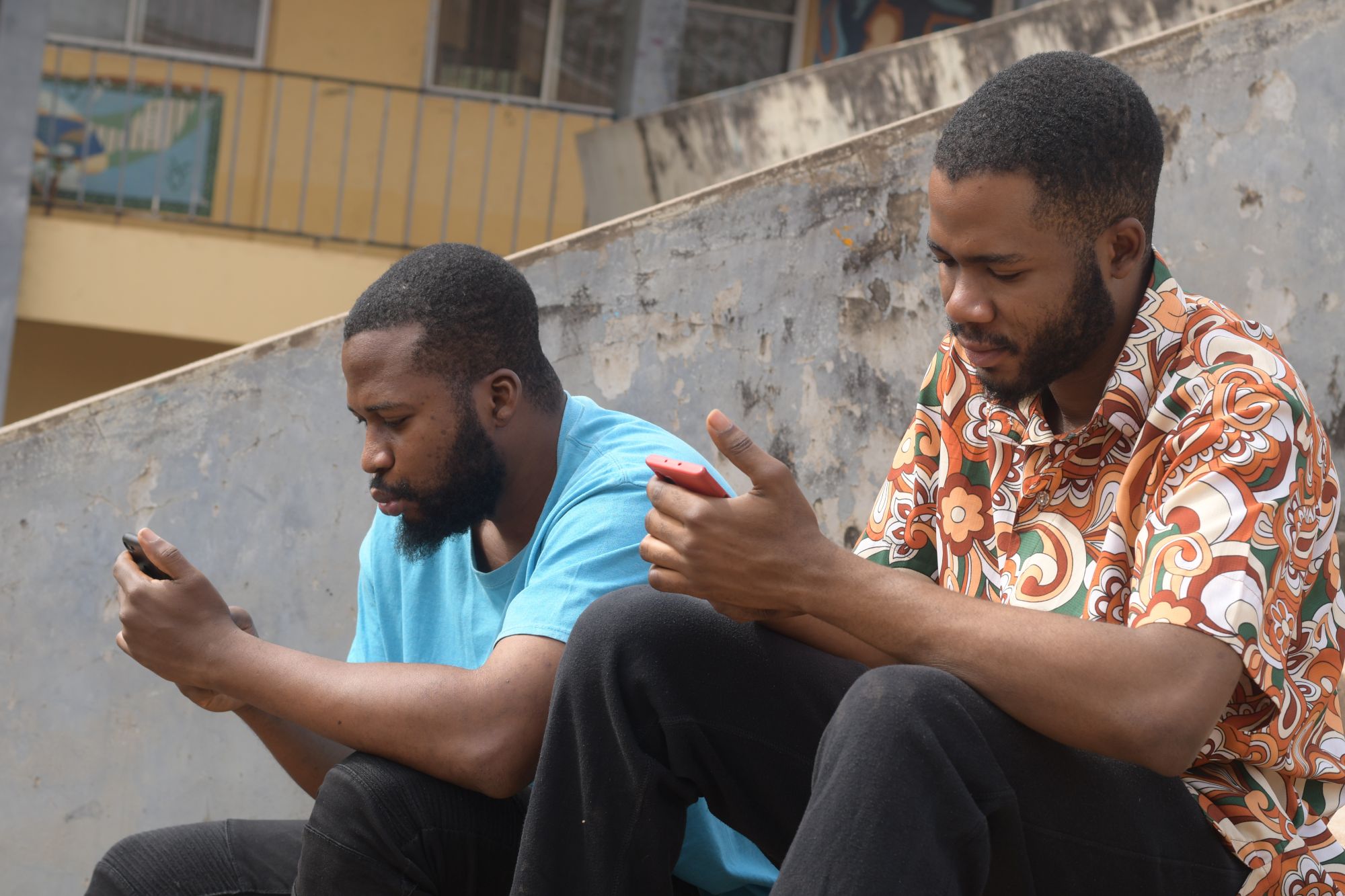 Two men set on concrete steps, looking at their phones with serious expressions