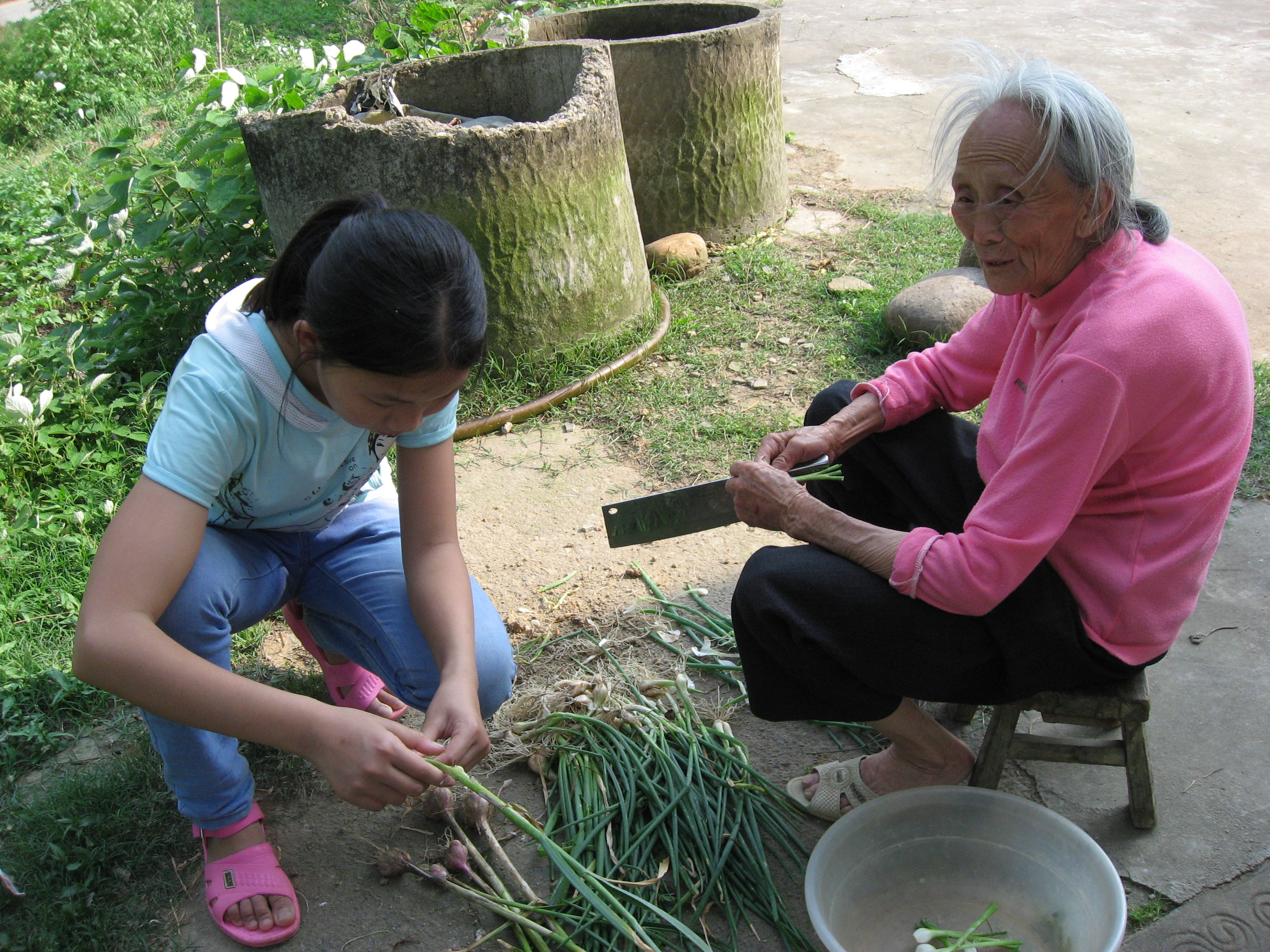 A young girl sat outside with her grandmother, helping with preparing vegetables
