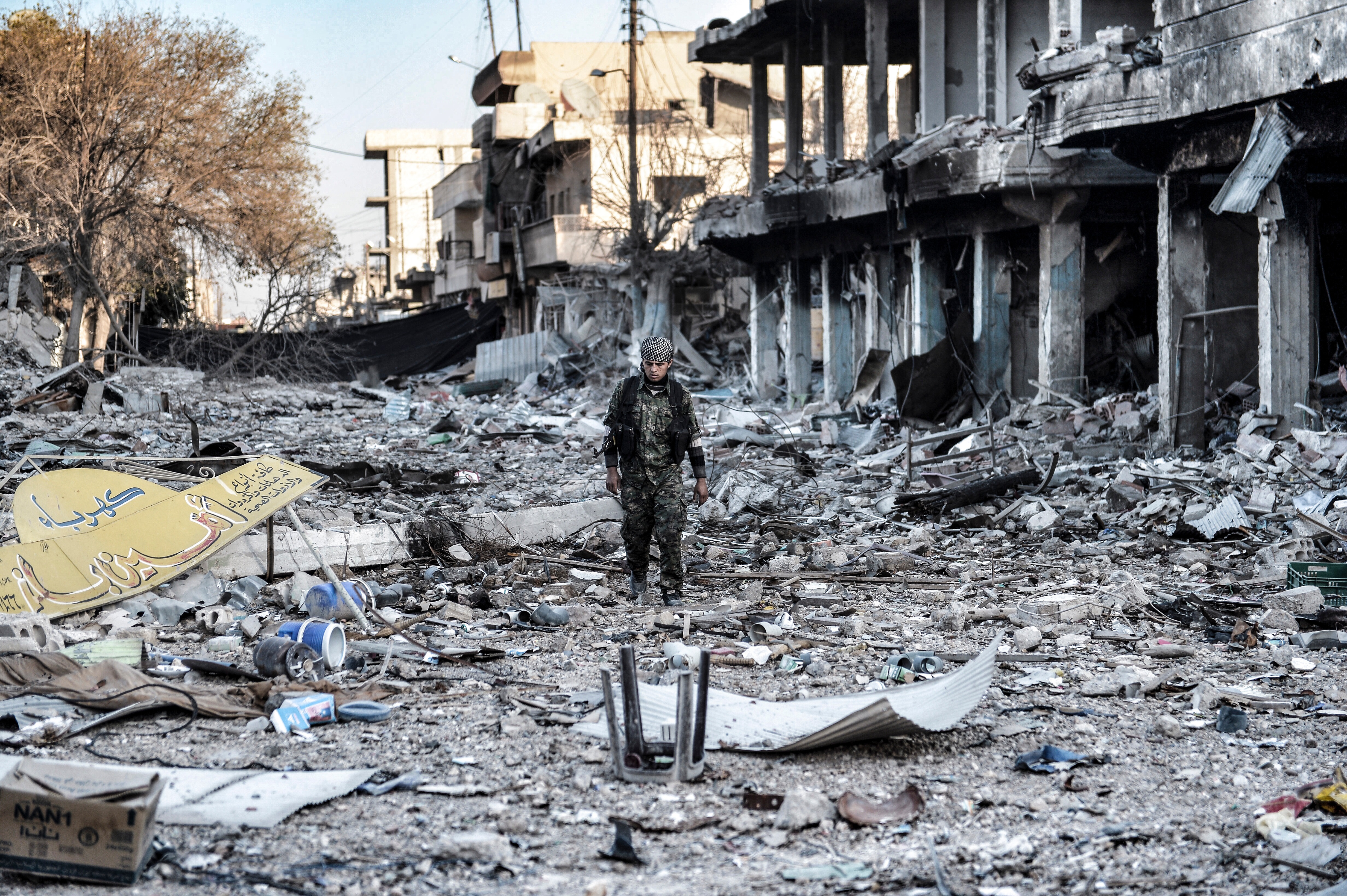 A soldier walks down a street filled with rubble from buildings