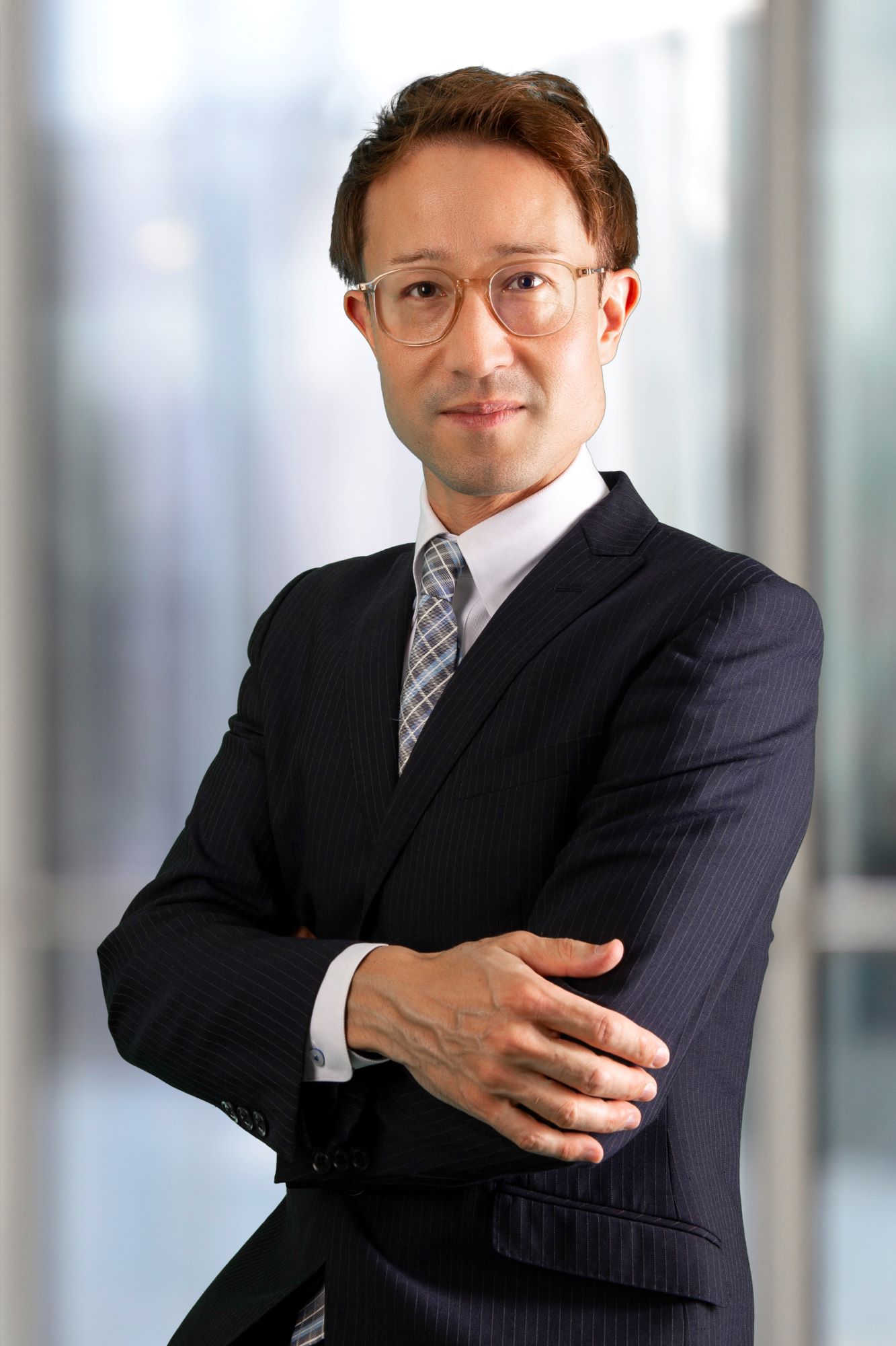 Dr Buchmeier has short brown hair and is wearing clear-rimmed glasses. He is wearing a pinstripe suit, shirt and tie. He is standing with his arms folded, looking at the camera. 