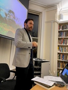Gregory Thaler standing at the front of a room, presenting in front of a screen