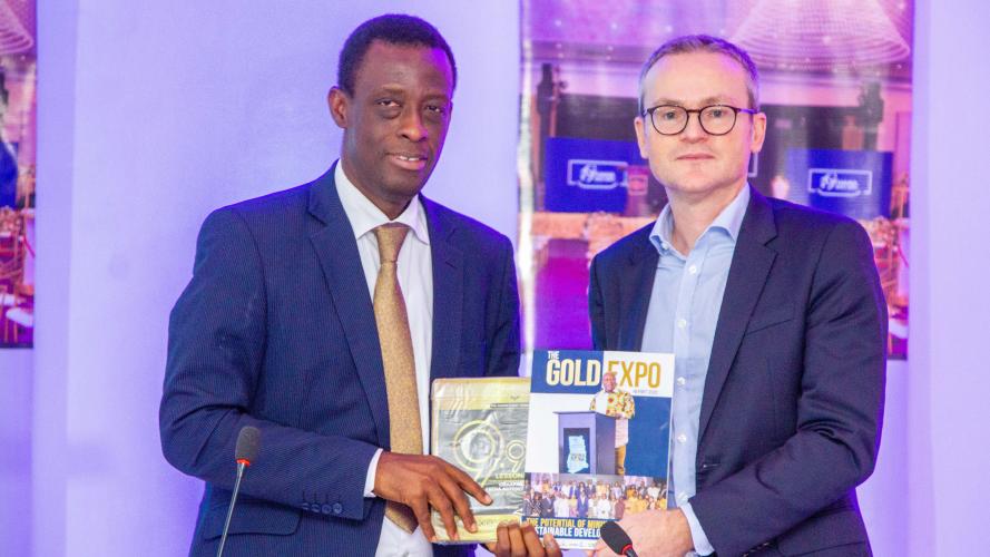 Two men in suits standing side by side, both holding a 'The Gold Expo' book.