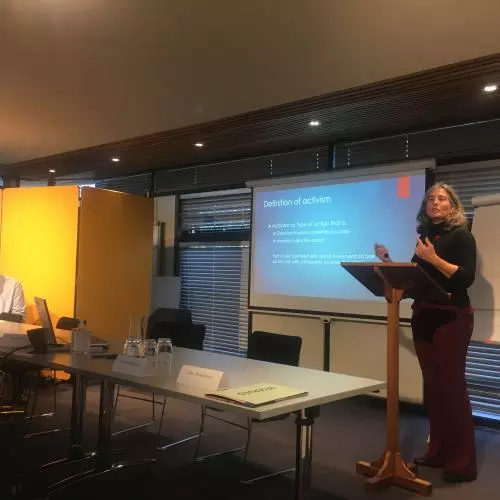 An academic standing on a stage, presenting in front of a projected presentation. 2020