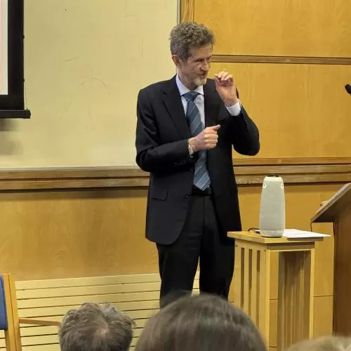 Professor Hugh Whittaker stands on a stage, presenting a lecture