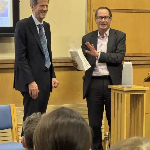 Professor Hugh Whittaker stands on a stage, being presented with a gift