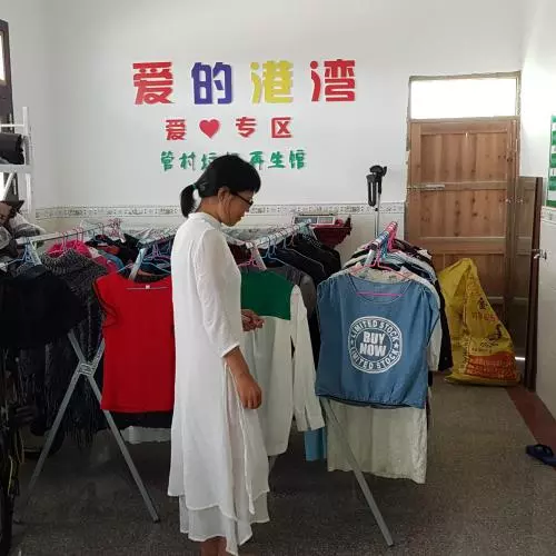 A lady with black hair tied back in a ponytail wearing a long white dress is looking at racks of clothing.