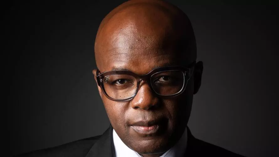 Profile photo of Miles Tendi wearing dark rimmed glasses, a white shirt, black suit and black tie 