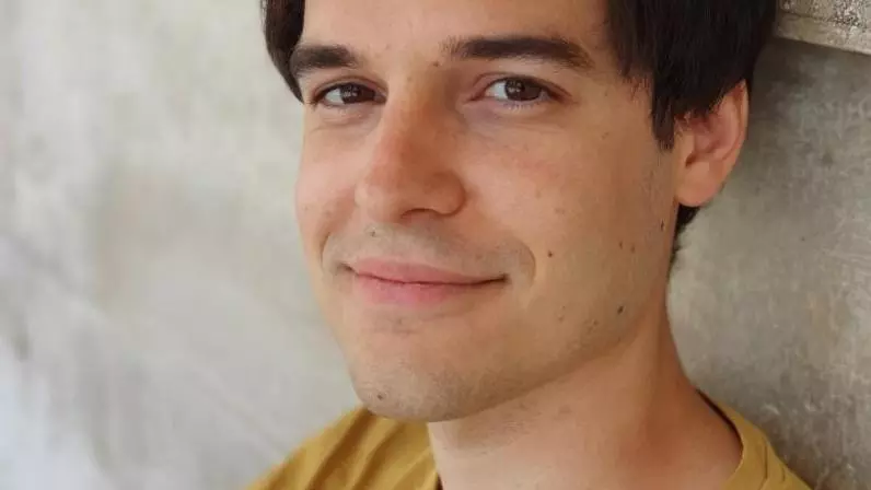 Marco has short brown hair and is wearing a yellow t shirt