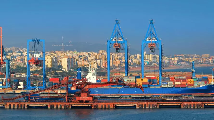 Visakhapatnam port, India. Ship in a cargo port with shipping containers on the dockside, view of a the city in the background.