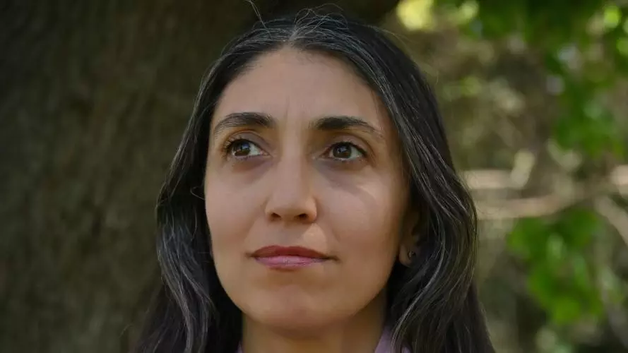 Dr Alice Gaya has long dark hair and is wearing a lilac scarf over a dark blouse. 