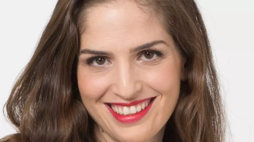 Dr Alfi-Nissan has long brown hair and brown eyes. She is smiling broadly at the camera.