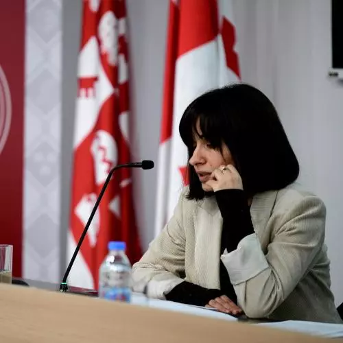 Dr Berikashvili has short black hair and is wearing a light grey blazer. She is leaning on a lectern, speaking into a microphone