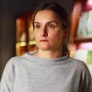 Dr Batiashvili is wearing a grey jumper and standing in front of a display cabinet, looking to the left of the camera