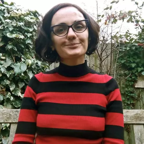 Salome Tsopurashvili has short dark hair and glasses. She is wearing a red and black striped top and is sat on a bench