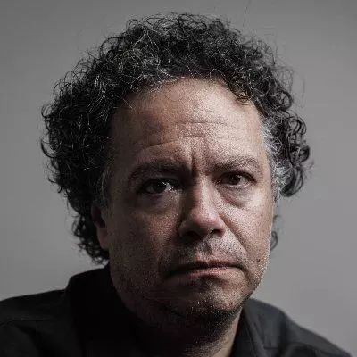 Oswaldo E. do Amaral has short curly dark hair. He is looking directly into the camera with his face partially in shadow