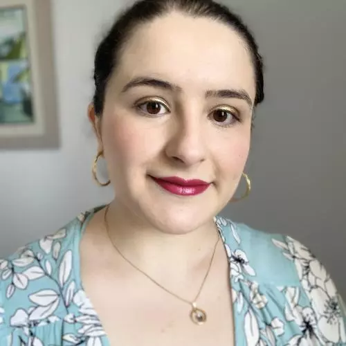 Loreno has her dark hair swept back from her face, and wearing gold hoop earrings. Her top is powder blue with white flower pattern.