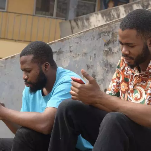 Two men set on concrete steps, looking at their phones with serious expressions