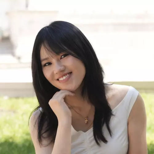  Mingdan has long black hair, is resting her chin on her hand, and is smiling at the camera. She's wearing a sleeveless white top