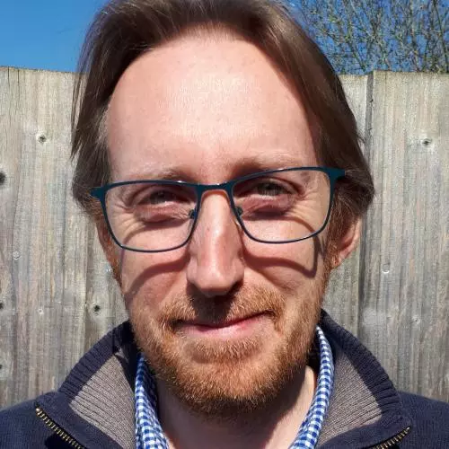 Jason Mosley has brown hair, beard and metal-framed glasses. He's wearing a blue and white checked shirt under a fleece jacket.  