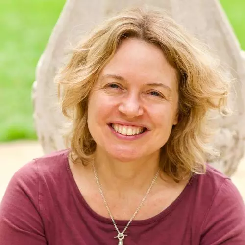 Rachel has shoulder-length blonde wavy hair and is smiling at the camera. She's wearing a ruby coloured top with silver pendant necklace