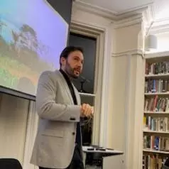 Gregory Thaler standing at the front of a room, presenting in front of a screen