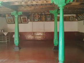 Interior view of a room with four green pillars in the centre. The right and back walls are lined with shelves displaying framed pictures 