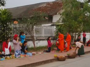 Buddhist monks in orange robes walking down a street lined with people
