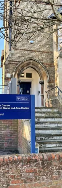 The African Studies Centre is a tall building made of light brick. It has large bay windows and a staircase leading to an arch before a porch. There is a new, dark blue sign outside the front with the Centre name. 