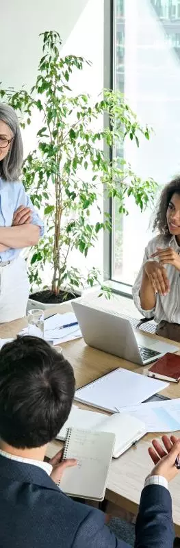 People around a table in a meeting room. The room has large window looking onto another building. 