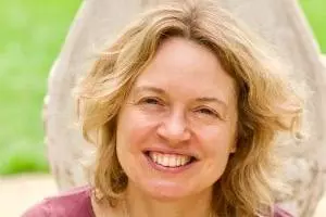 Rachel has shoulder-length blonde wavy hair and is smiling at the camera. She's wearing a ruby coloured top with silver pendant necklace