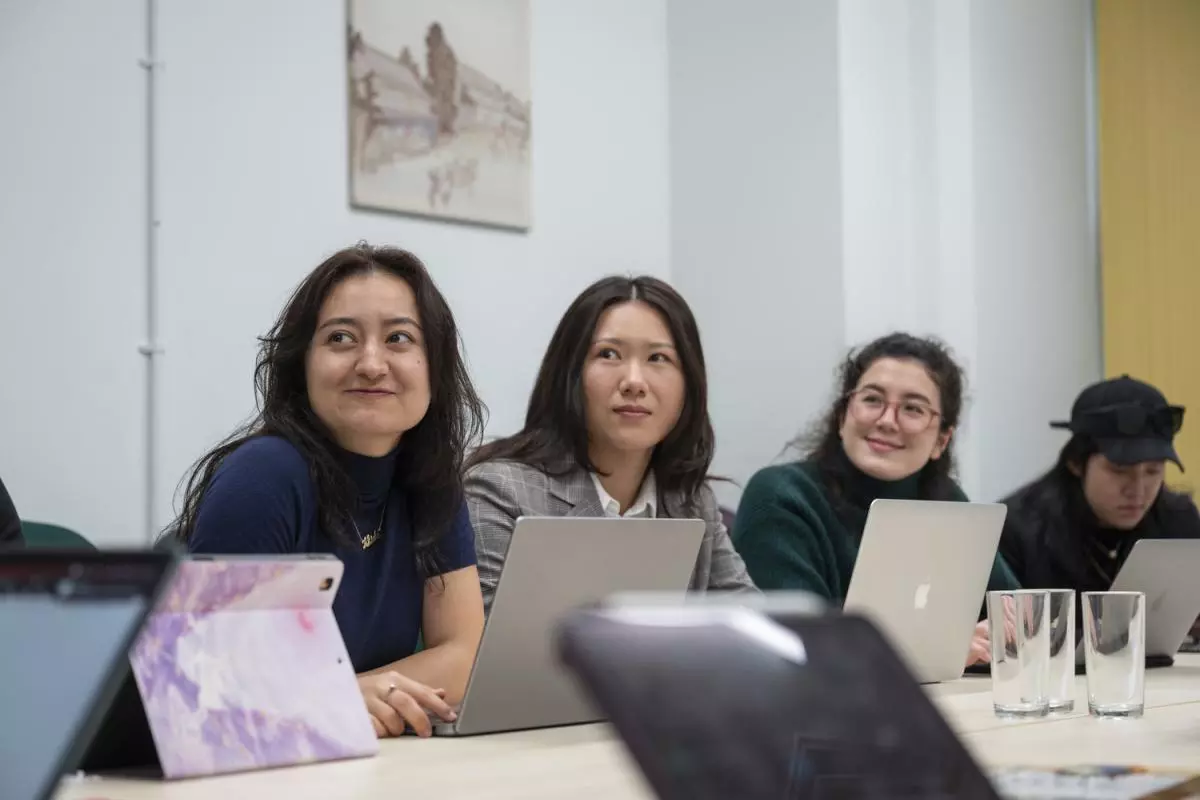 Three students sitting side by side at a table, with laptops open in front of them