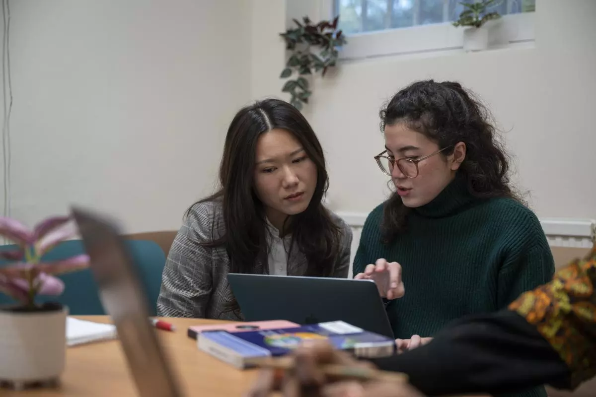 Two academics sitting on a sofa, looking at a laptop. The person on the right is speaking and gesturing at the screen.