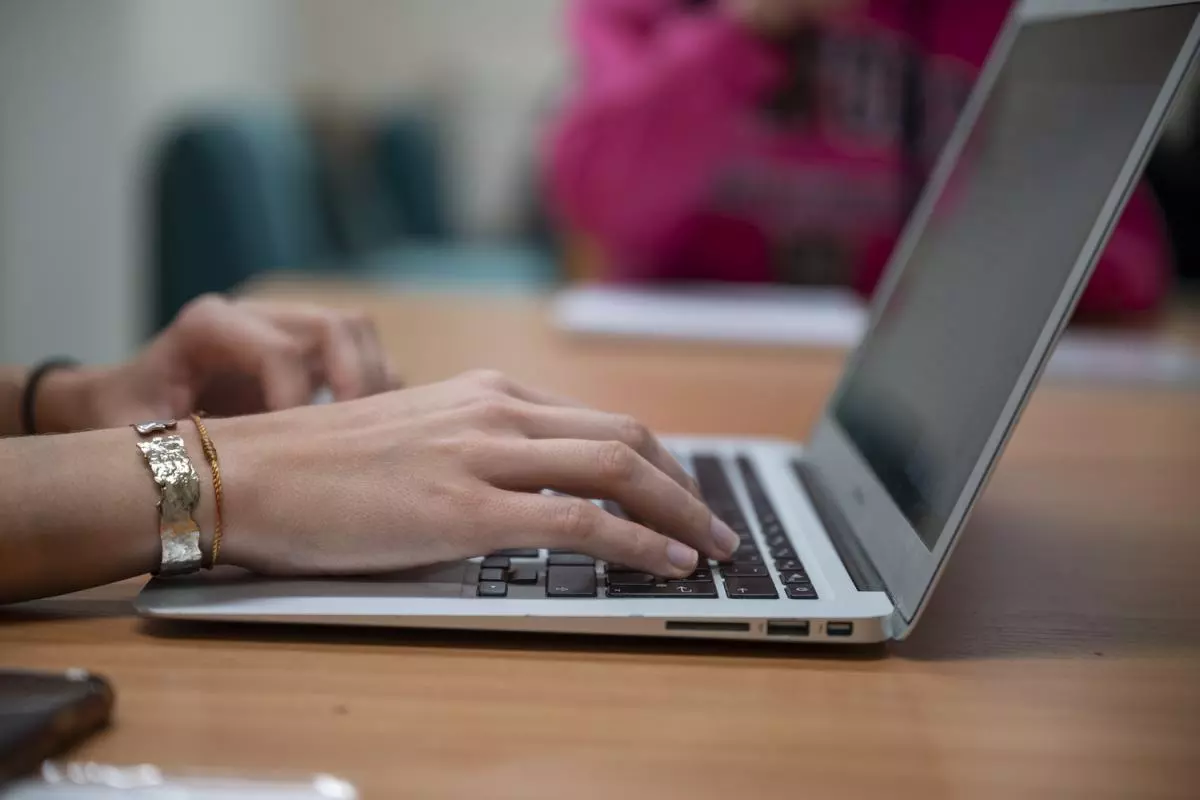 A close up of hands typing at a laptop. The student is wearing two metal bangles on their wrist.