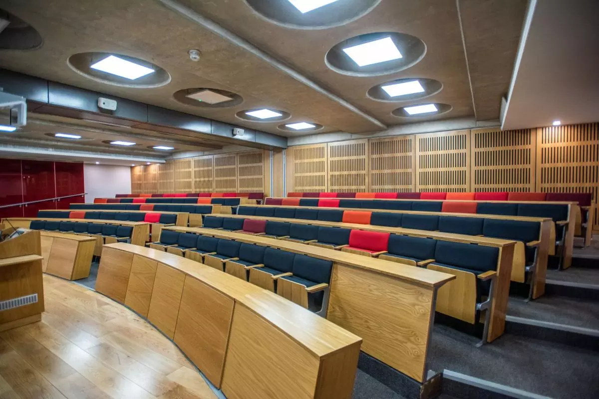 A large modern lecture room, with cushioned seats arranged in curved rows behind wooden desks.